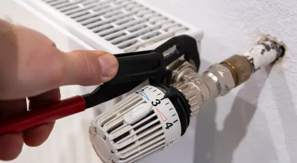 Hand uses pliers to heizungsventil tauschen. Der Thermostatkopf ist auf Stufe 3 eingestellt.