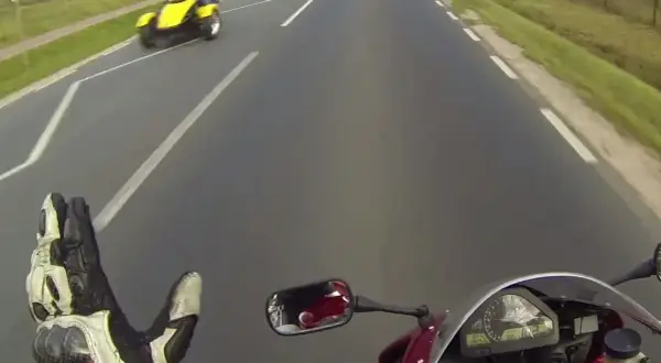 Pozdrowienie motocyklistów na drodze. Żółty pojazd trójkołowy mija motocyklistę.