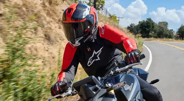 Motocyklista w czerwono-czarnym kasku i kurtce jedzie po krętej drodze.