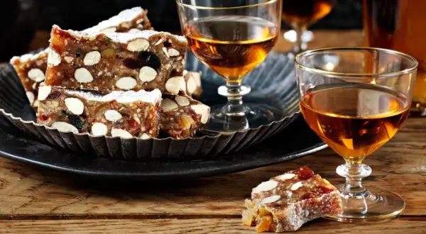 Panforte-bitar med mandlar och torkad frukt, pudrade med florsocker, serveras med ett glas gyllene likör. Ett härligt panforte recept att njuta av.
