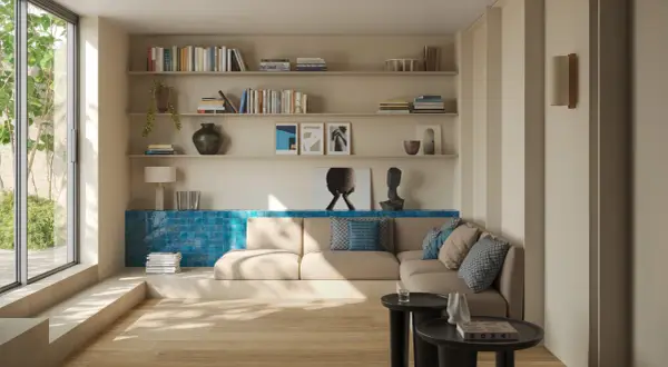 Ein heller Boden trifft auf eine warme, sandfarbene Wandfarbe. Ein gemütliches Wohnzimmer mit Bücherregalen, einem Sofa und einem großen Fenster.