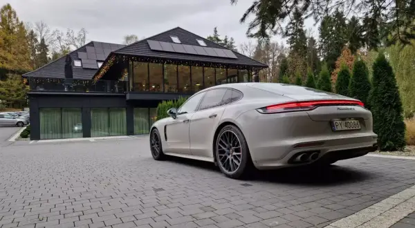 Białe Porsche Panamera GTS przed nowoczesnym budynkiem z panelami słonecznymi. Idealny wybór dla firm ceniących leasing operacyjny.