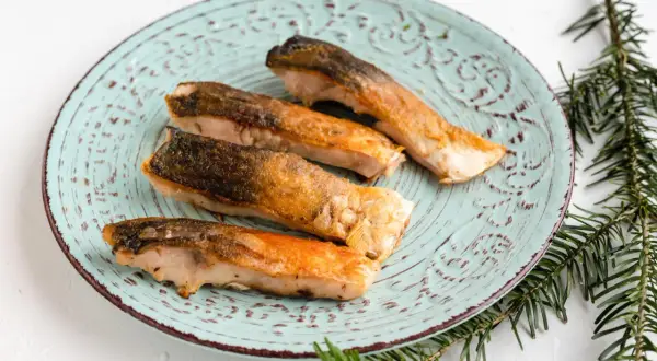 Vier goldbraun gebratene Karpfenfilets mit Haut liegen auf einem mintgrünen Teller.