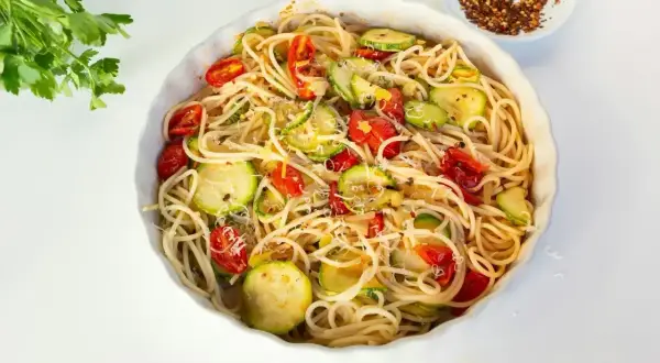 Makaron spaghetti z cukinią i pomidorkami koktajlowymi, posypany parmezanem.