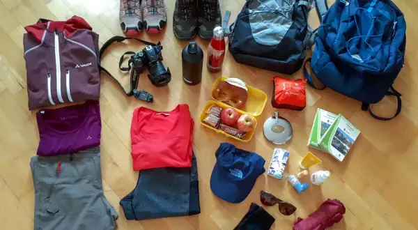 Packliste Wanderurlaub: Wanderschuhe, Rucksäcke, Kleidung, Kamera, Verpflegung und Karten für ein Abenteuer in den Bergen.