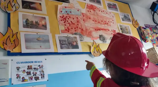 Niña con casco de bombero señala un mural de bomberos, parte de originales proyectos infantiles.