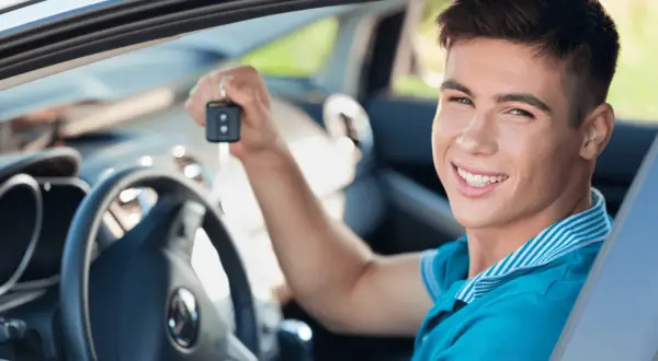 Uśmiechnięty młody mężczyzna trzyma kluczyki do swojego pierwszego auta. Idealne jakie auto na pierwsze!