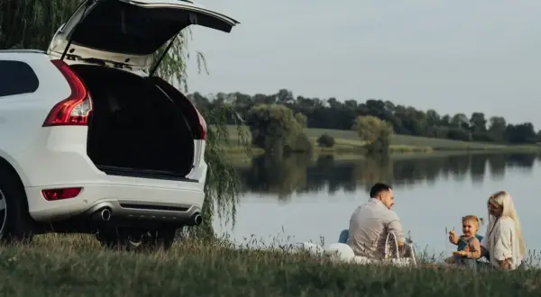 Rodzina cieszy się piknikiem nad jeziorem, planując długie weekendy 2026. Otwarty bagażnik białego SUV-a sugeruje gotowość na przygodę.