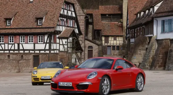 Dwa Porsche, czerwone i żółte, stoją przed zabytkowymi domami. Czy to PDK?