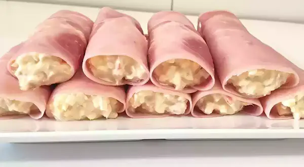 Rollitos de jamón york rellenos de ensaladilla cremosa, presentados en una bandeja blanca.