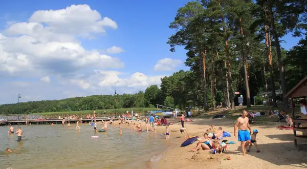 Słoneczny dzień nad jeziorem w Augustowie. Ludzie kąpią się, opalają na plaży i spacerują po molo.