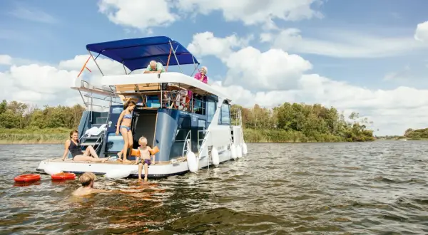 Familie auf einem Hausboot in der Mecklenburgischen Seenplatte, einige schwimmen, andere entspannen sich.
