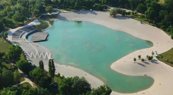 Zagrzeb plaża z turkusową wodą i piaszczystymi brzegami, otoczona zielenią. Widoczne amfiteatr i drewniany pomost.