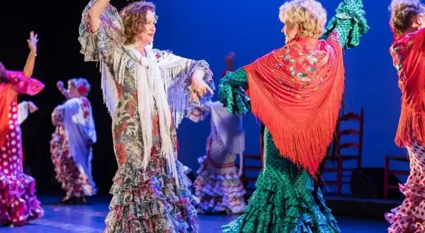 Dos mujeres bailan sevillanas, con volantes y mantones, evocando el origen de esta danza.