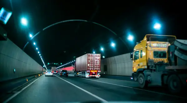 Camion jaune et conteneur dans un tunnel éclairé. La circulation suit la réglementation poids lourd.