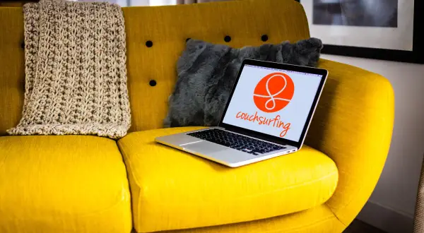 Żółta kanapa z laptopem otwartym na stronie couchsurfing. Obok koc i szara poduszka.