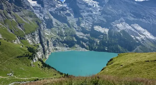 Türkisblaue Oeschinensee Schweiz, umrahmt von steilen, grünen Berghängen und schneebedeckten Gipfeln. Ein idyllischer Ort für Wanderer.