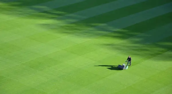 Greenkeeper praca: mężczyzna kosi trawnik na boisku sportowym, tworząc idealne pasy.