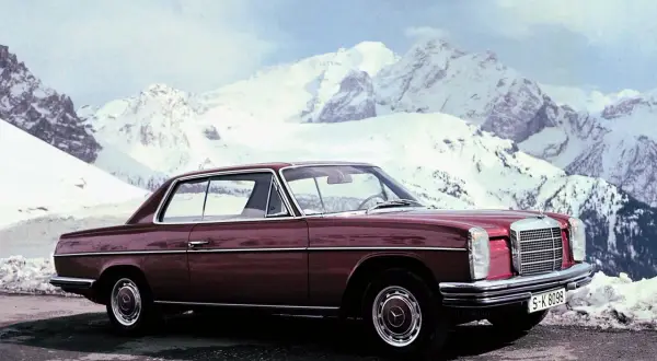 Ciemnoczerwony Mercedes W114 coupe na tle ośnieżonych gór. Klasyka motoryzacji w zimowej scenerii.