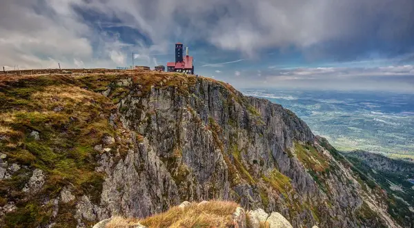 Budynek na szczycie skalistego, trawiastego zbocza górskiego z widokiem na dolinę.