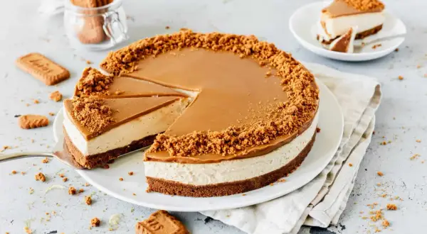 Ein köstlicher Lotus Cheesecake mit Karamellglasur und Keksbröseln. Ein Stück wurde bereits entnommen.