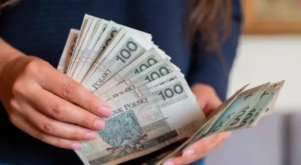 Dłonie trzymające stos banknotów 100 zł. Czy to przedpłata, czy zaliczka? Decyzja o płatności.