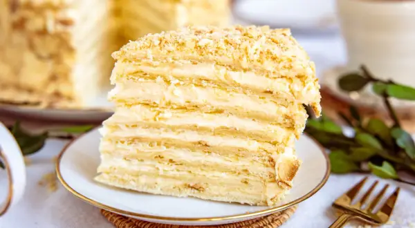 Ein Stück Napoleon Torte mit vielen Schichten Blätterteig und cremiger Füllung, bestreut mit Krümeln.