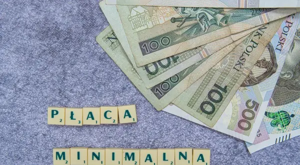 Polskie banknoty 100 zł i 500 zł ułożone wachlarzowo, obok kafelki z napisami "PŁACA" i "MINIMALNA".