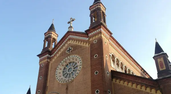 La chiesa San Dalmazzo a Torino, con le sue torri e il rosone, si staglia contro il cielo azzurro.