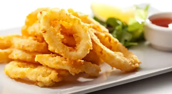 Anelli di totano dorati e croccanti, cotti in friggitrice ad aria, serviti su un piatto bianco con contorno di insalata e salsa.