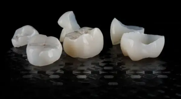 Kilka białych, ceramicznych koron dentystycznych leży na czarnym, błyszczącym tle.