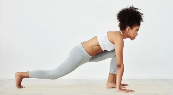 Woman in athletic wear performs a low lunge, stretching her upper body after a workout.