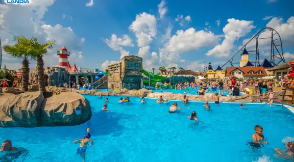 Energylandia wodne atrakcje: ludzie kąpią się w basenie, zjeżdżalnie i roller coaster w tle.