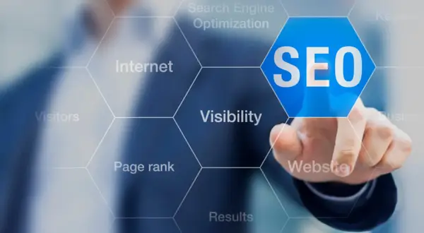 Palec wskazuje na niebieski sześciokąt z napisem SEO. Wokół widoczne są hasła: Internet, Search Engine Optimization, Keywords, Visibility, Website, Results, Page rank, Visitors. To podpowiedź, jak zbadac element.