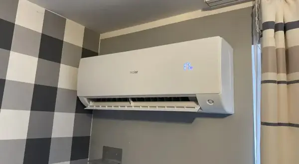 Biała klimatyzacja Haier zamontowana na szarej ścianie, obok wzorzystej tapety i zasłon.