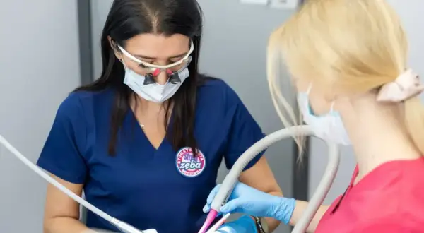 Dentystka z lupami i maską przygotowuje znieczulenie dentystyczne skład. Asystentka trzyma ssak.