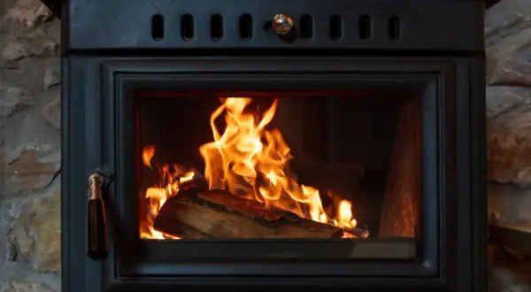 Un feu crépite dans un poêle à bois, le branchement poele a bois est discret derrière la pierre.