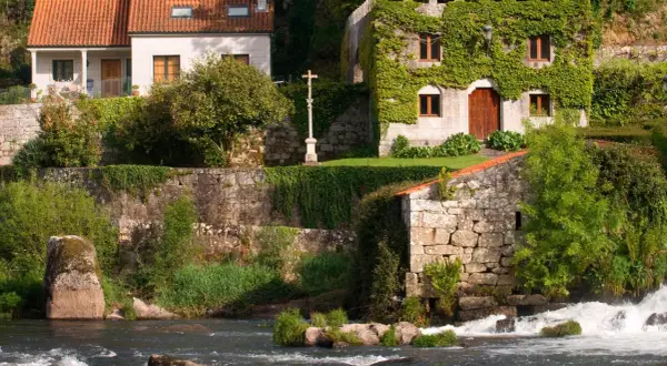 El pazo de Ponte Maceira, con su arquitectura de piedra y vegetación exuberante, se alza junto a un río de aguas bravas.
