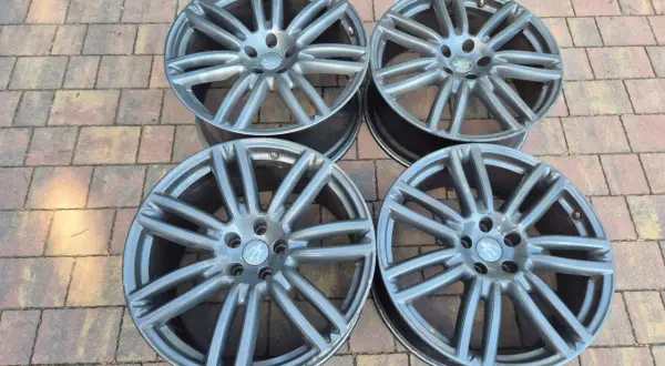 Cztery felgi do Maserati Ghibli SQ4, szare, z charakterystycznym wzorem, leżą na kostce brukowej.