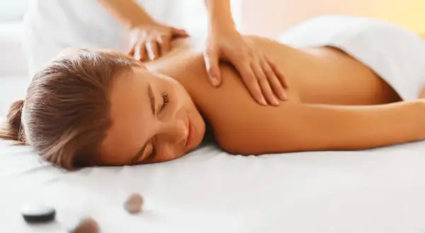 Kobieta leży na białym łóżku, a fizjoterapeuta masuje jej plecy.