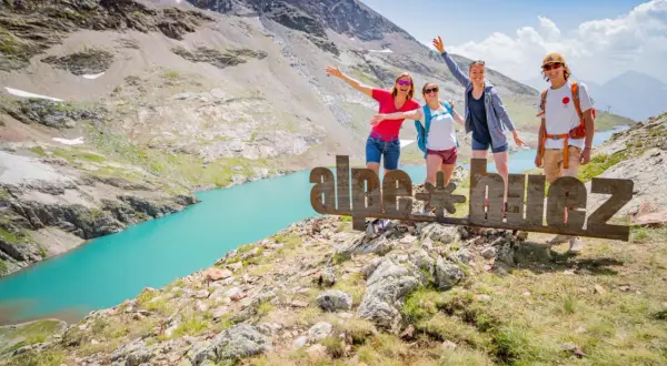 Quatre amis profitent de leurs vacances d'été dans les Alpes, près d'un lac turquoise. Ils posent devant un panneau "alpe d'huez".