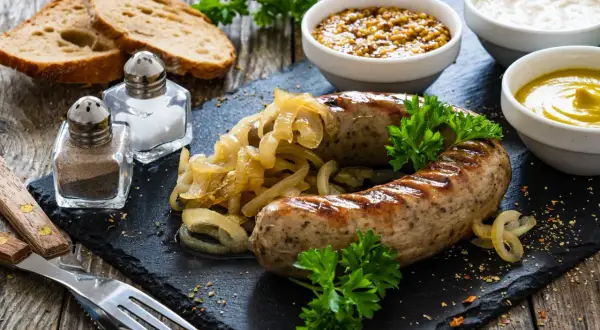 Pyszna biała kiełbasa pieczona w cebuli i musztardzie, podana z chlebem i sosami.