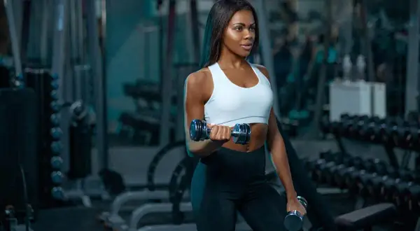 A woman with muscular arms lifts dumbbells in a gym, showcasing her dedication to fitness.