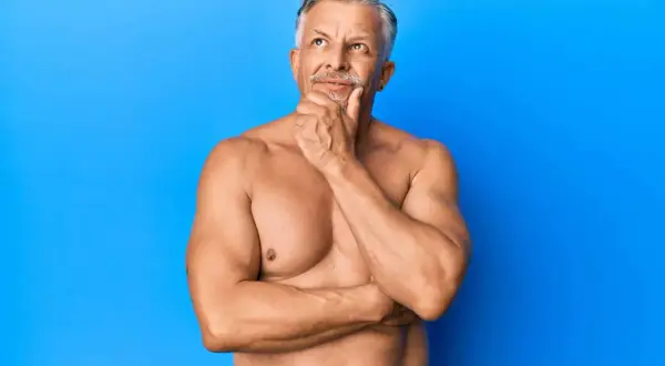 Ein nachdenklicher Mann mit grauen Haaren und Bart, dessen Oberkörper trainiert ist, was auf gut entwickelte Typ 1 Muskelfasern hindeutet.