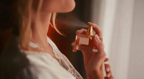 Kobieta rozpyla perfumy na szyję, wiedząc, gdzie pryskać perfumami, by zapach utrzymał się dłużej.