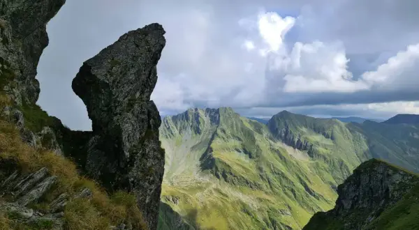 Steile Felsformationen und grüne Berghänge im Rahmen einer **Karpaten Wanderung**. Dramatische Wolkenformationen über den Gipfeln.
