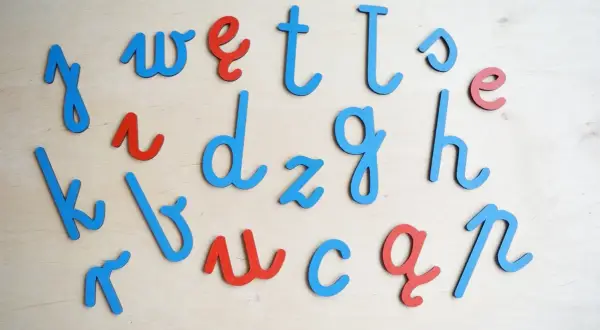 Drewniane litery alfabetu łacińskiego w kolorach niebieskim i czerwonym, ułożone na drewnianym tle.