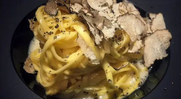 Tagliatelle al tartufo, un piatto elegante con pasta fresca condita con una cremosa salsa e generosamente guarnita con scaglie di tartufo nero.