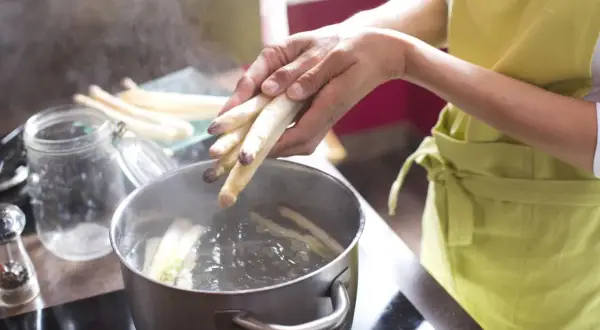 Hände legen weißen Spargel in kochendes Wasser. So wird gefrorener Spargel kochen.