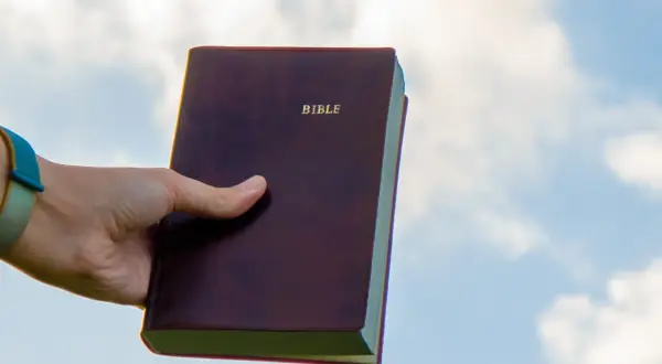 Dłoń trzyma Biblię na tle nieba. Czy to znaczy "Deus Deus Kosmateus"?